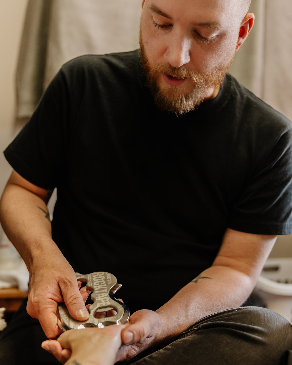 Mathieu Boudreau, RMT, seated beside the treatment table, explaining as he applies a stainless steel IASTM tool along a client's forearm.